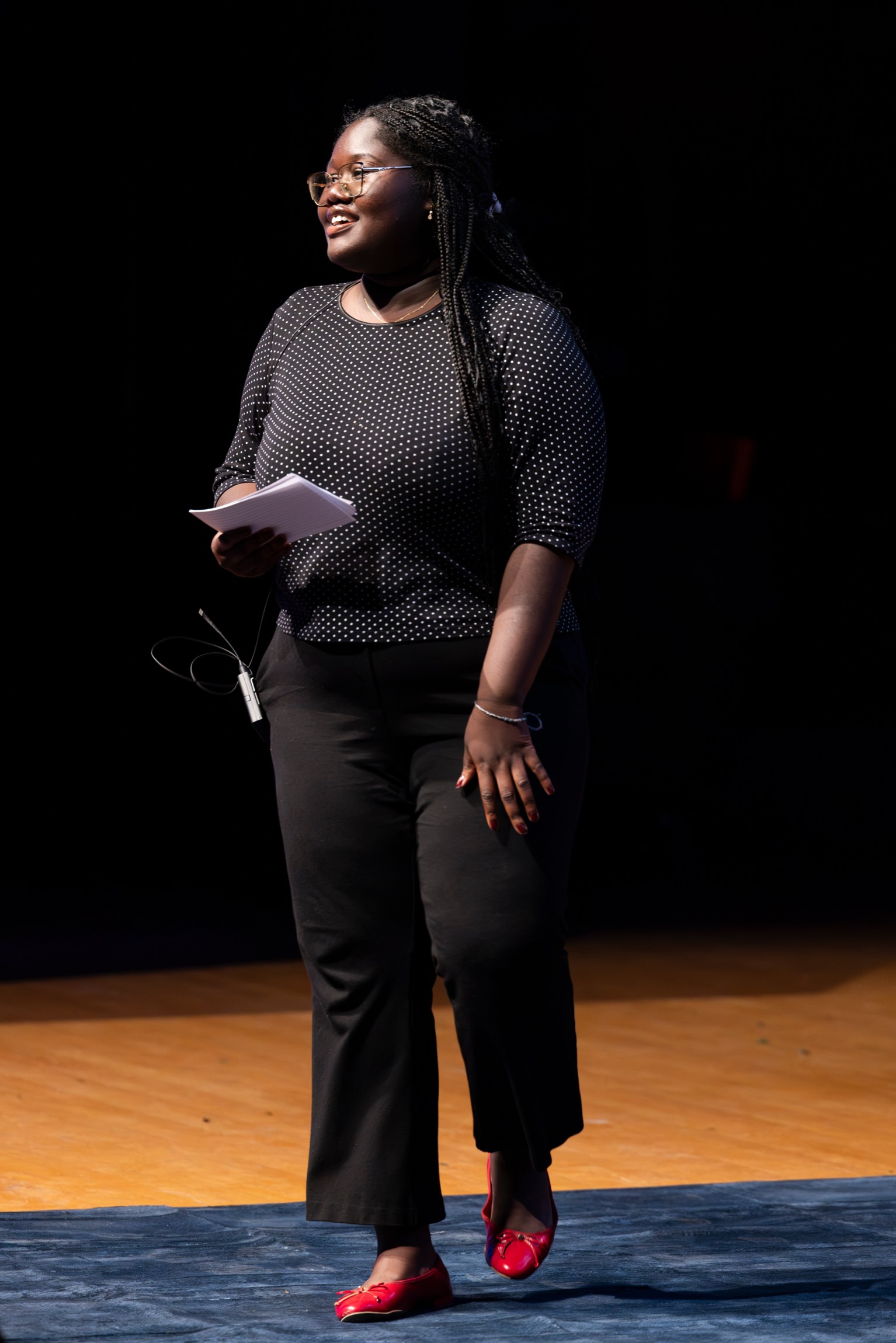 One woman stands on a stage and holds her notes to present to the crowd. 