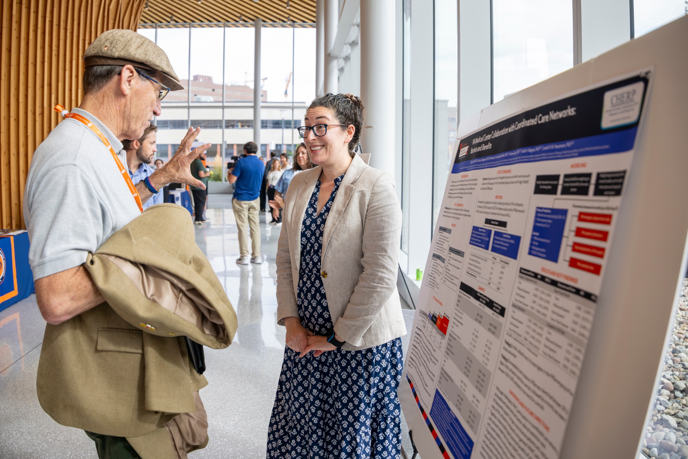 A man speaks to an enthusiastic researcher presenting her poster. 