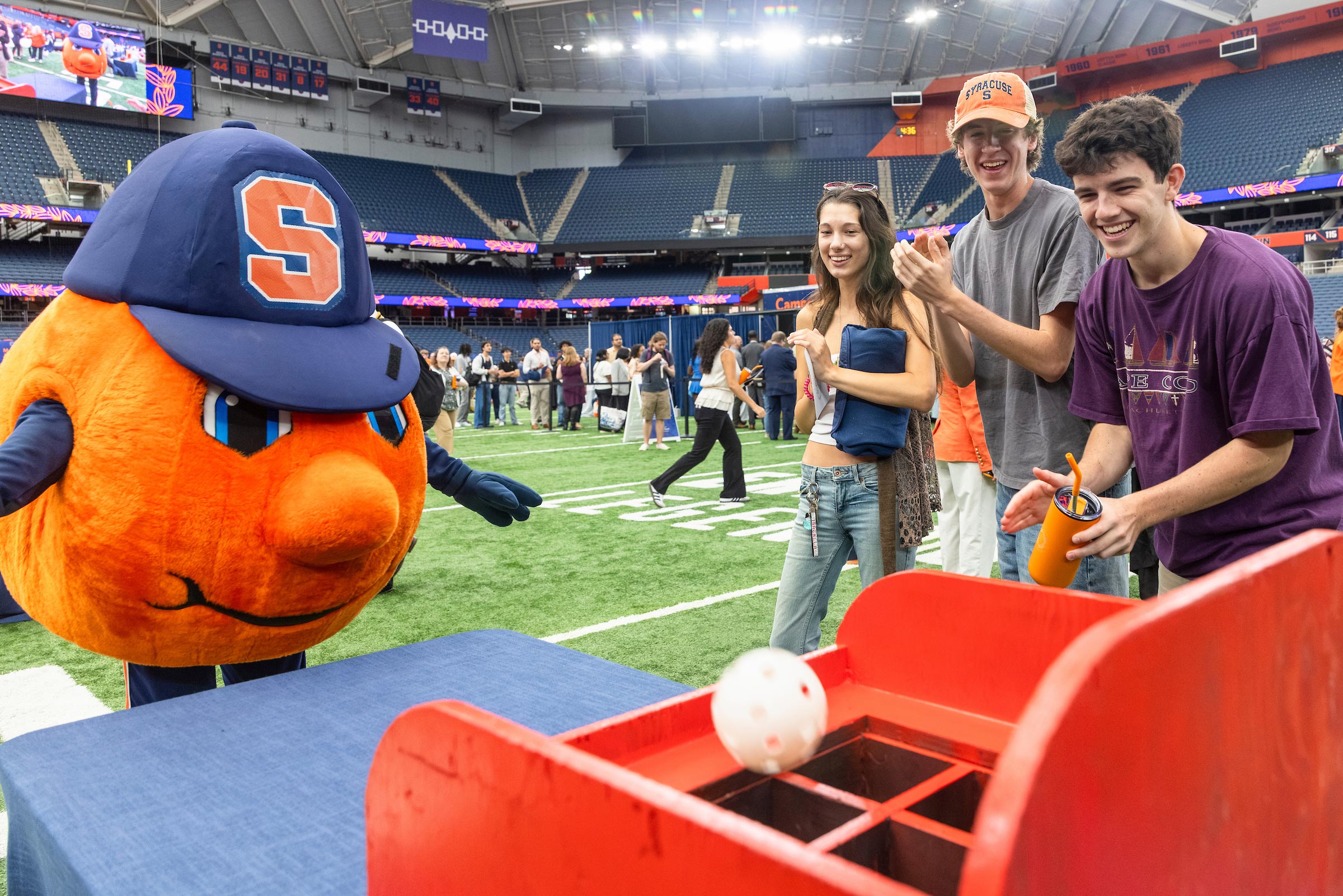 Three students cheer on Otto as they play one of the games at OrangeFest.