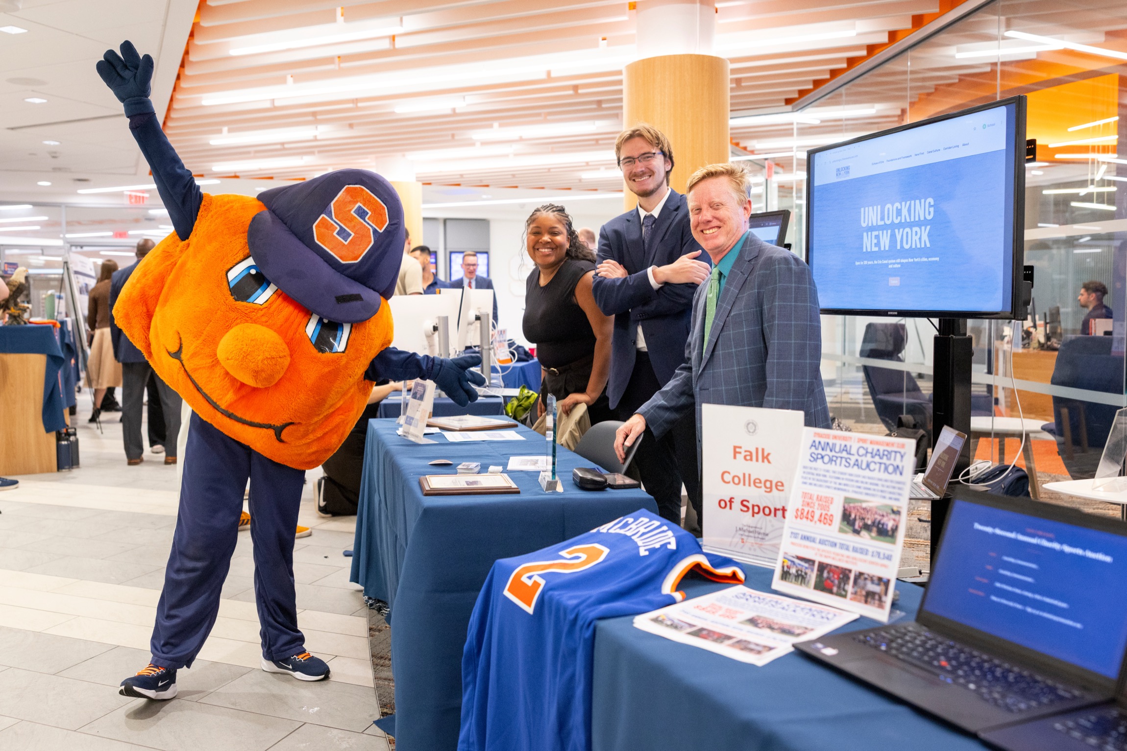 Otto the Orange poses with three people who are hosting a table at an event. 