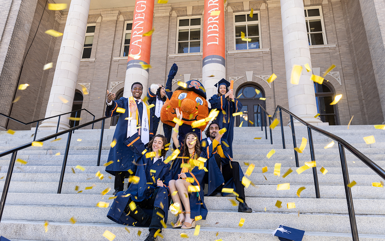 Students sitting on steps celebrating with Otto in confetti 