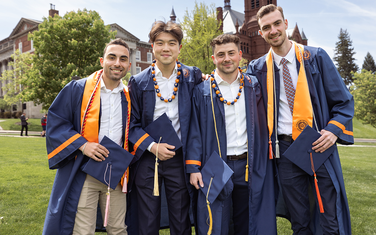 Four graduates in regalia on campus