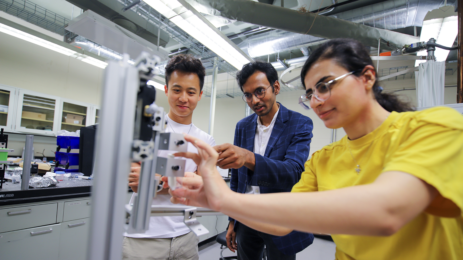 Professor Anupam Padney with two students examining metal equipment