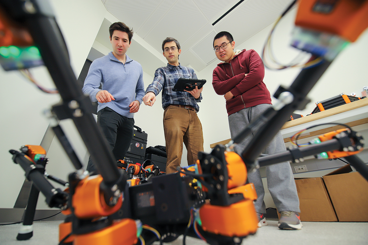 Three men standing and pointing at a drone