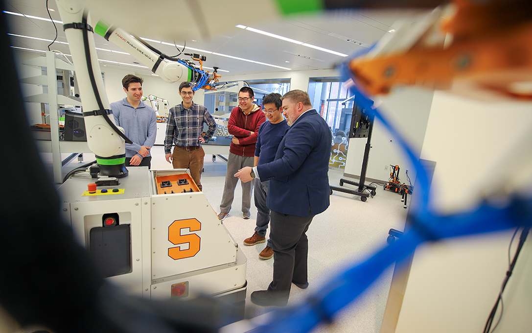 Professors Garrett Katz Yizhi Liu Zhenyu Gan and Alex K Jones and a student stand looking a piece of equipment