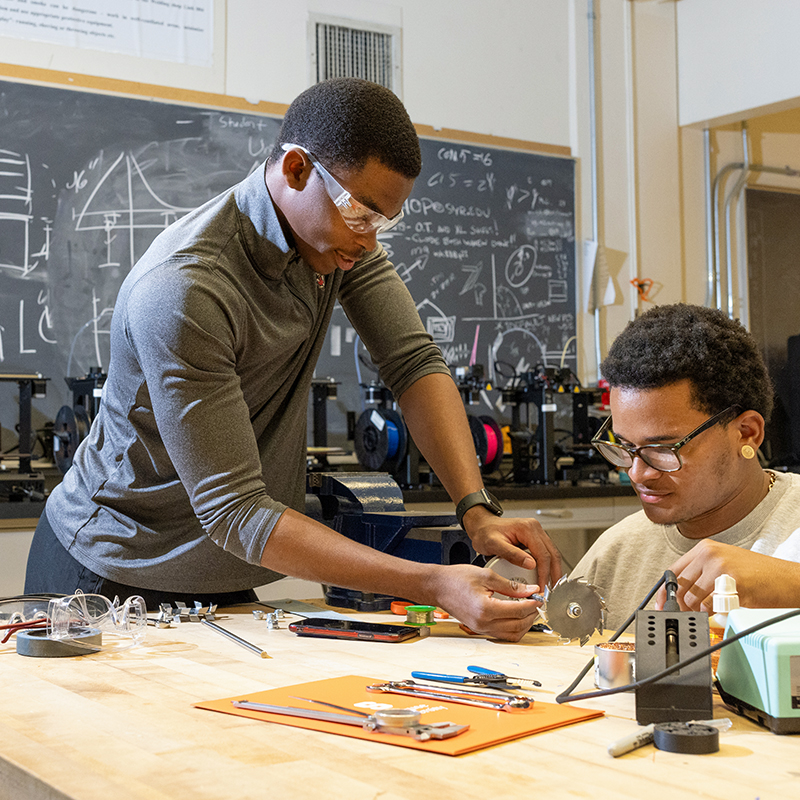Gabriel Ffatade stands and Ethan Yankee sits in a machine shop
