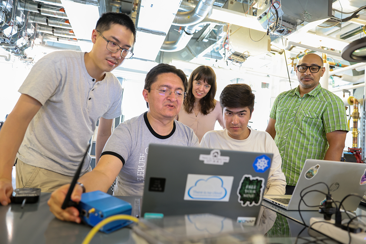 Porfessor Liz Carter and four students standing and looking at a laptop