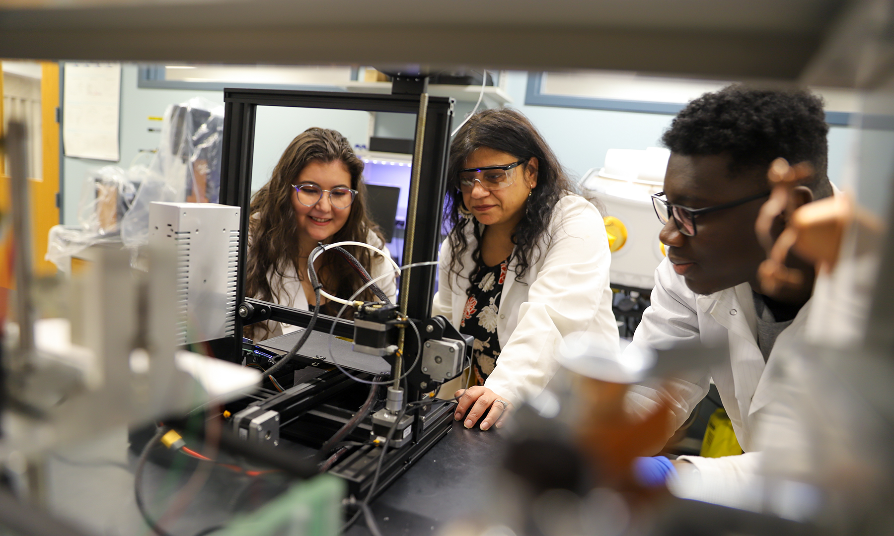 Two women and one man looking at a 3-D printer