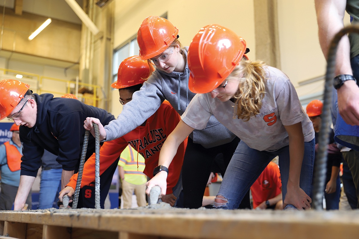 Four people wearing hard hats stir concrete