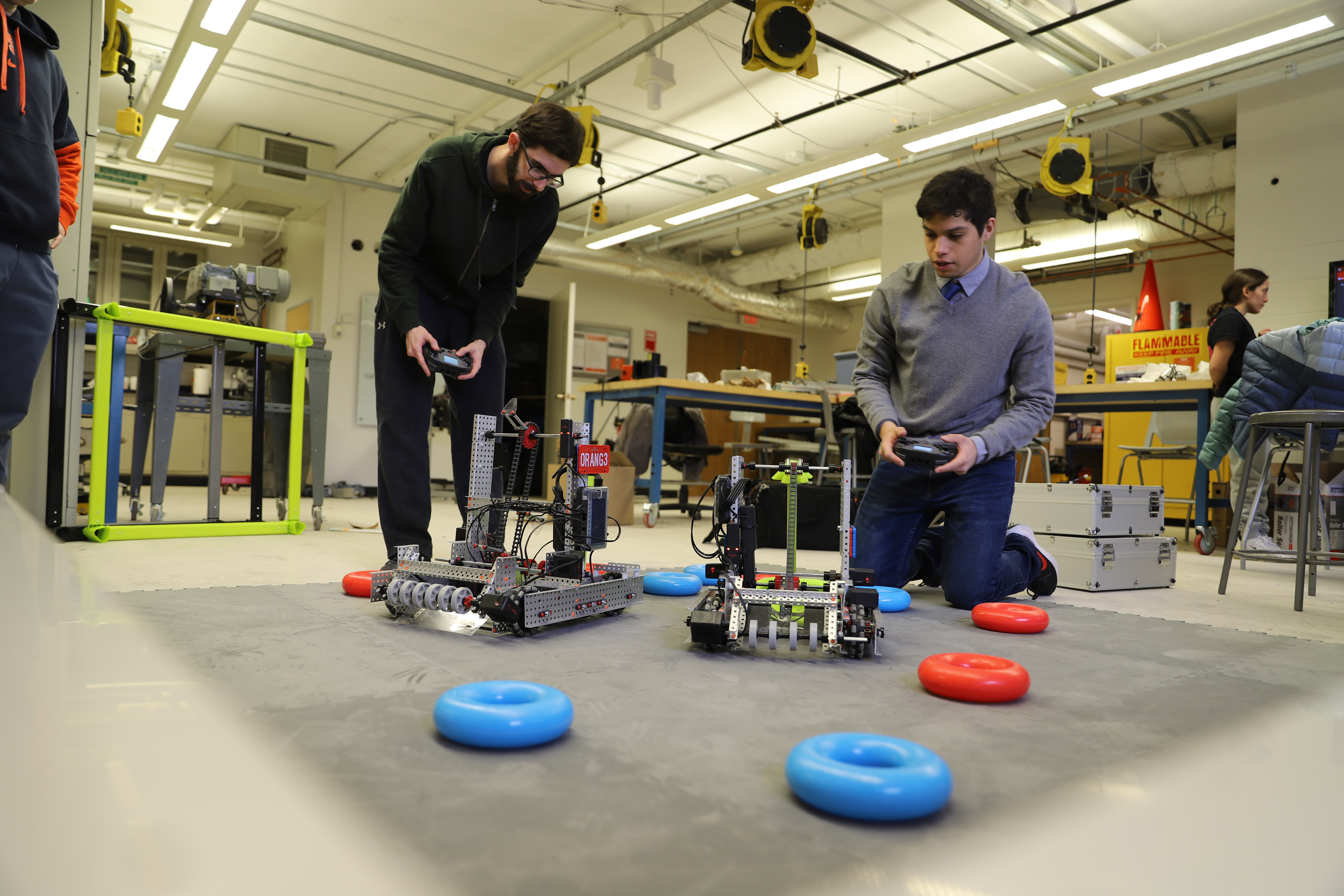 Two men holding remote controls and two robots