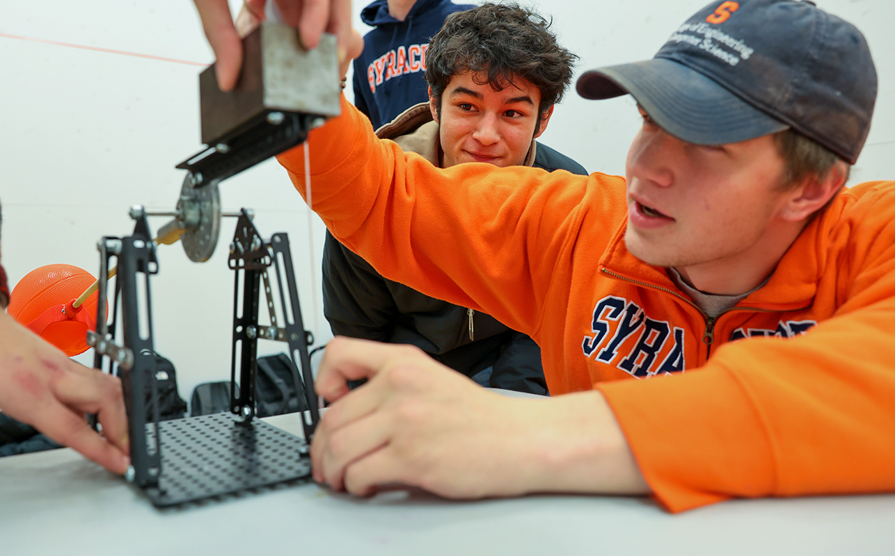 A boy adjusting a mechanical device while another boy looks on