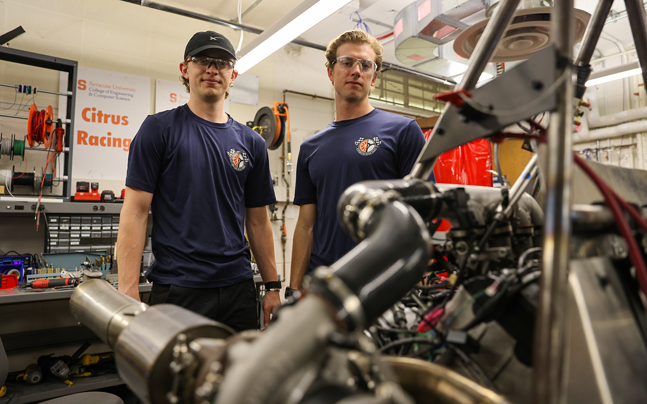 Two men standing behind a car engine