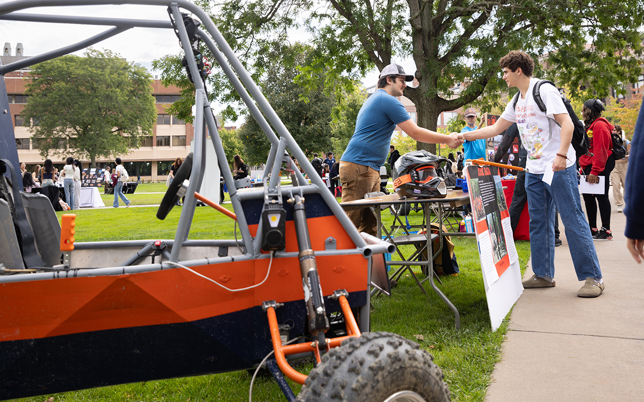 Two men shaking hands next to an offroad vehicle 