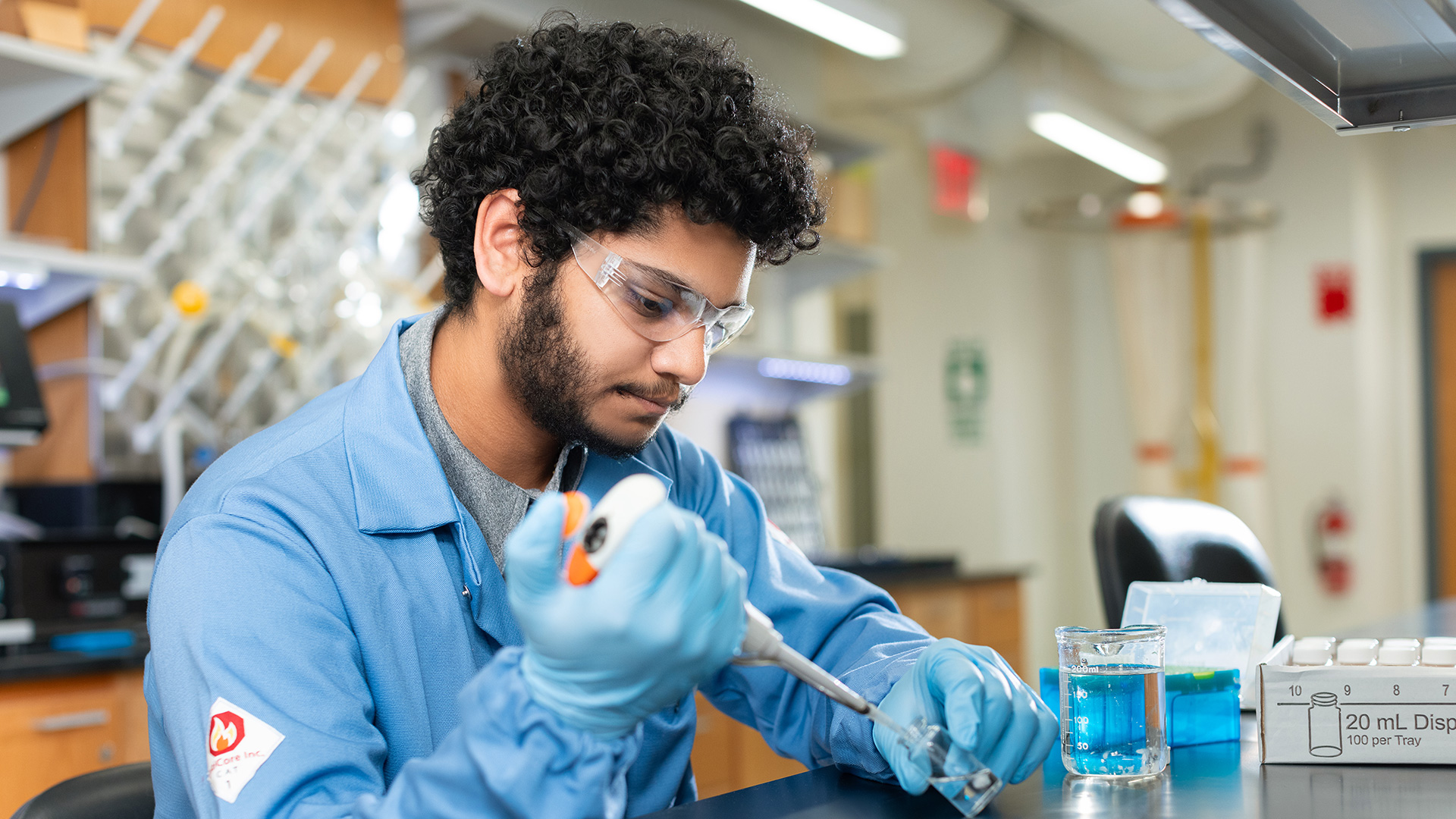 A man in a lab coat sitting at a table injecting liquid into a container