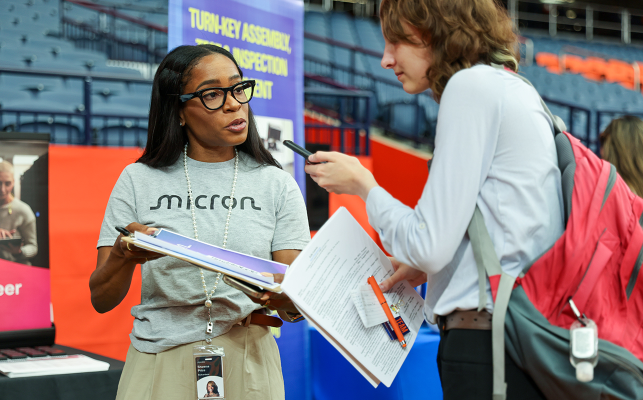 Two women standing, one holding a piece of paper, the other holding a phone