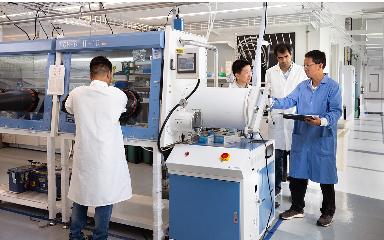 Four men standing in a laboratory looking at equipment 