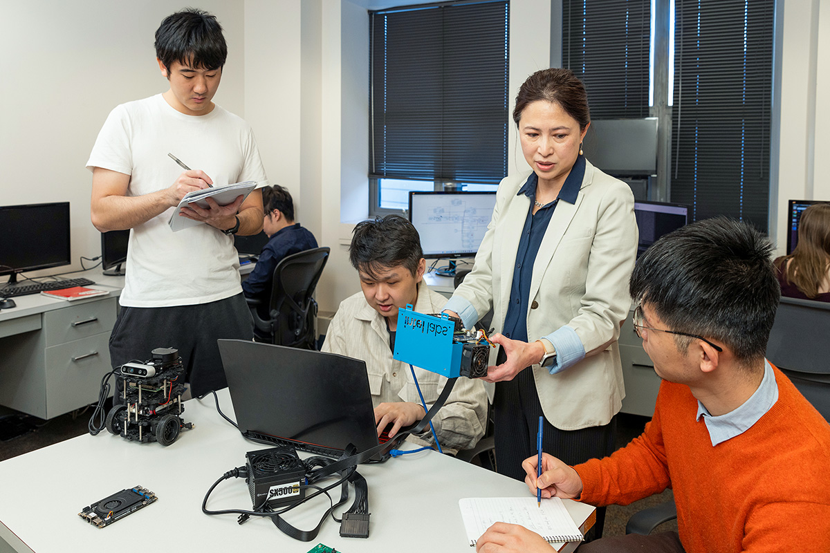 Professor Qinru Qiu holding electronic equipment and the men look at a computer