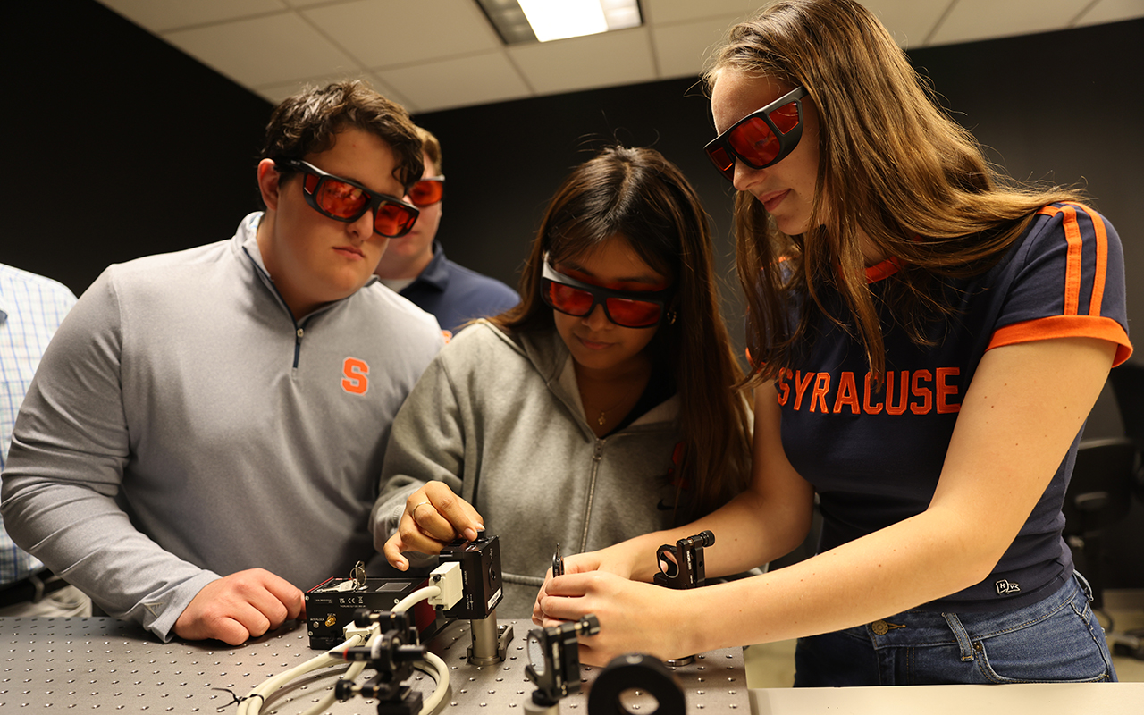 A man and two women adjust a piece of electronic equipment