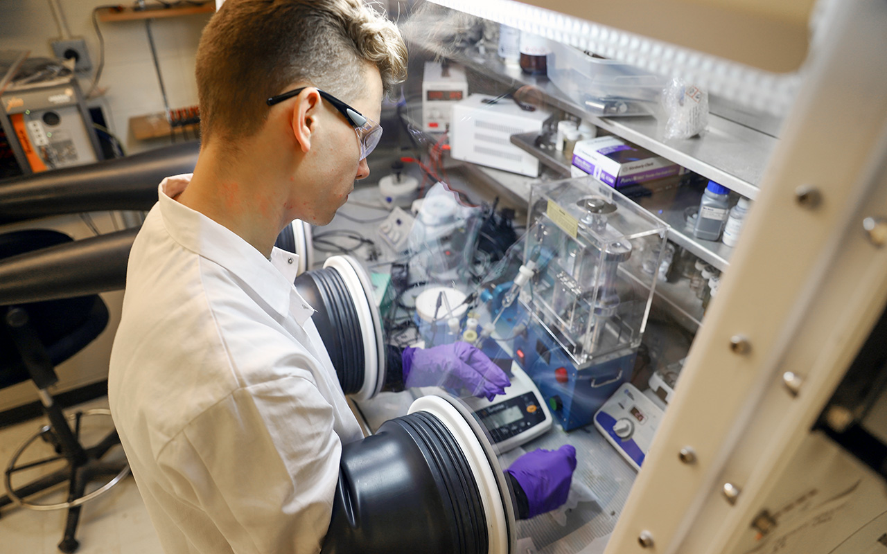 A man handling material in a lab under a safety hood