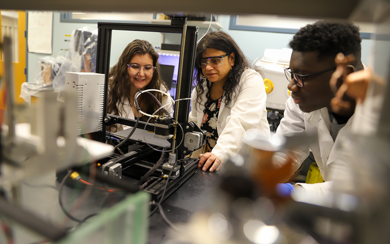 Two women and a man in a lab looking at a piece of equipment