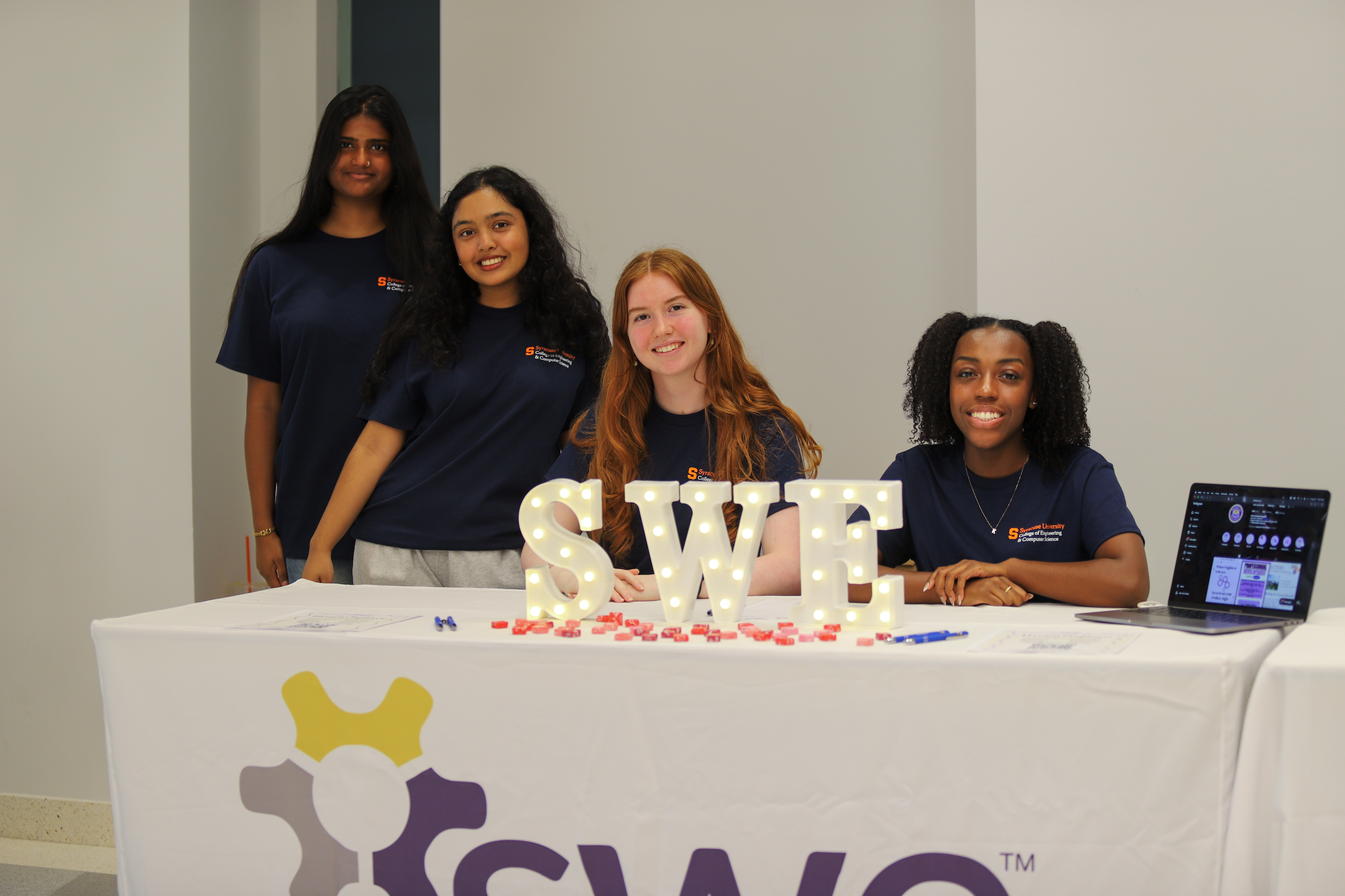 Two women standing and two women sitting at a table