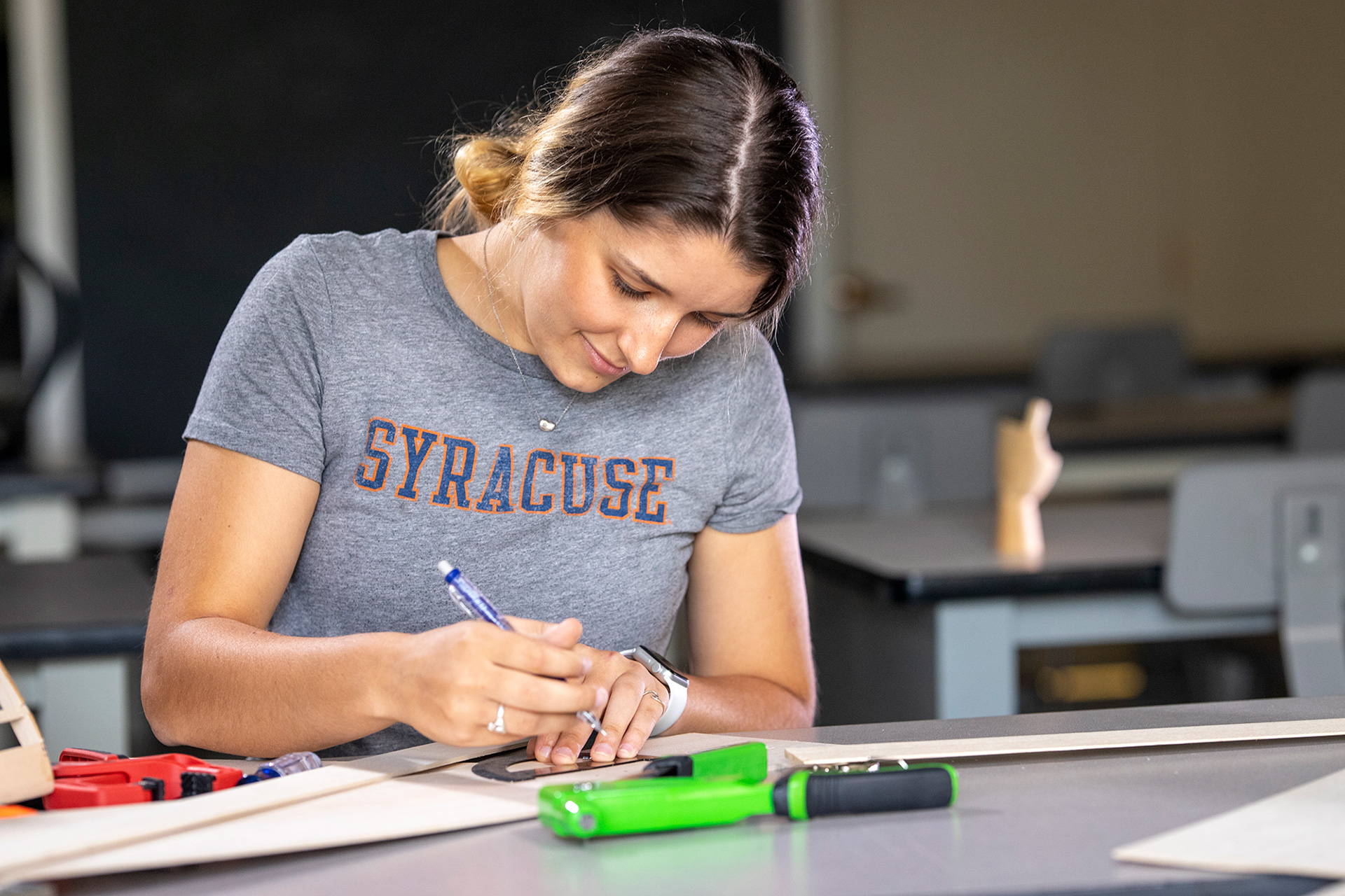 A girl sitting and writing in the shirt that says Syracuse