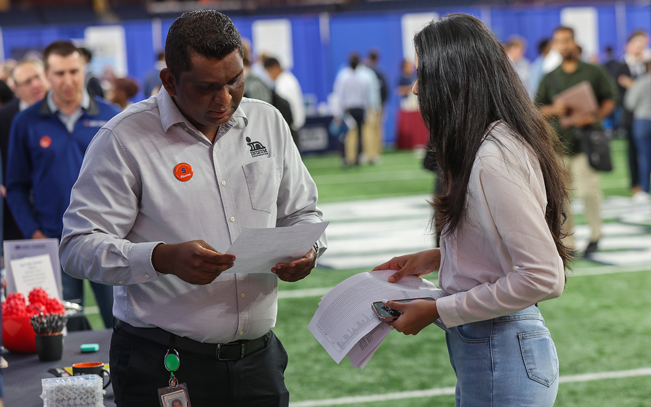 A man and a woman standing looking a pieces of paper.