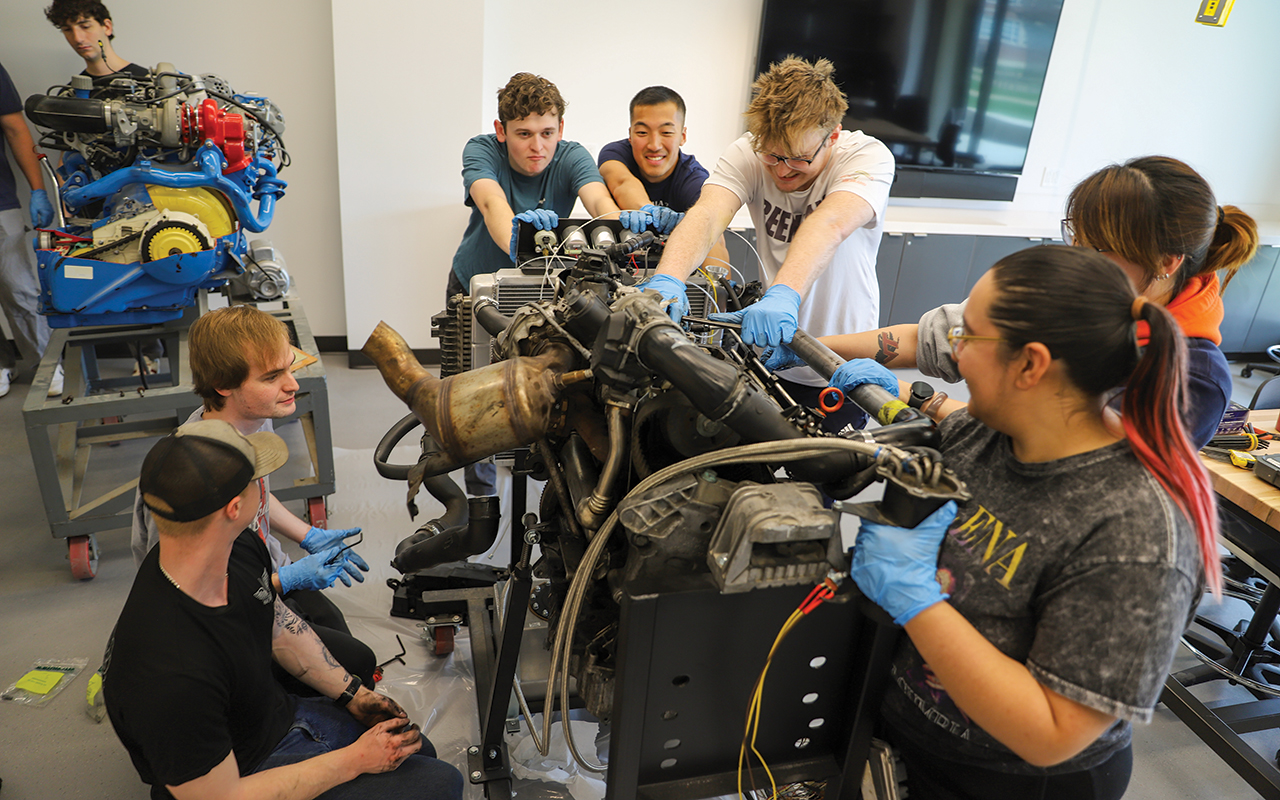 Seven students working on a car engine.