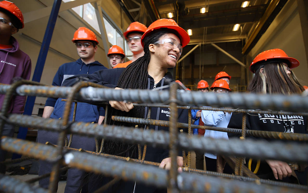 A group of people in orange hardhats standing behind a met a structure