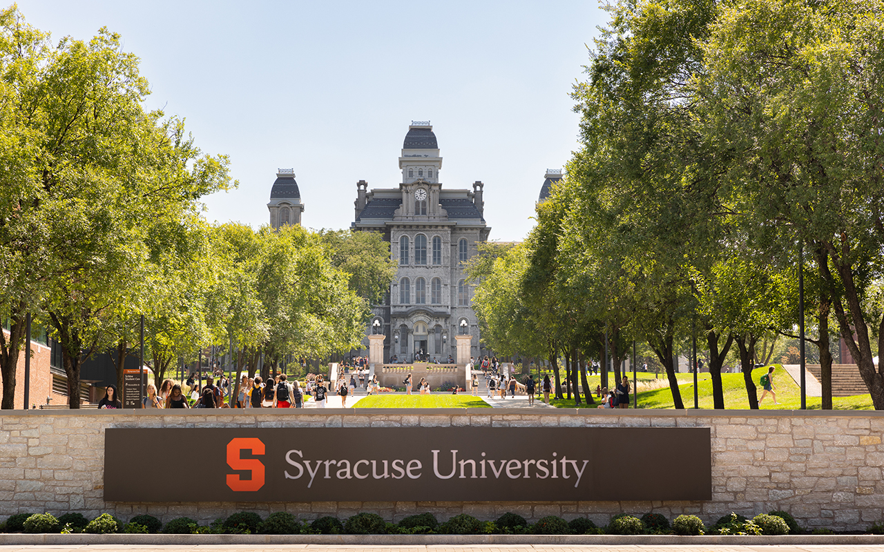 A gothic building with a sign in front of it that says Syracuse University.