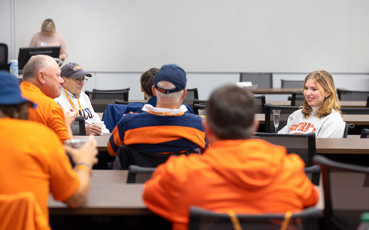A girl sitting talking to a room of people.