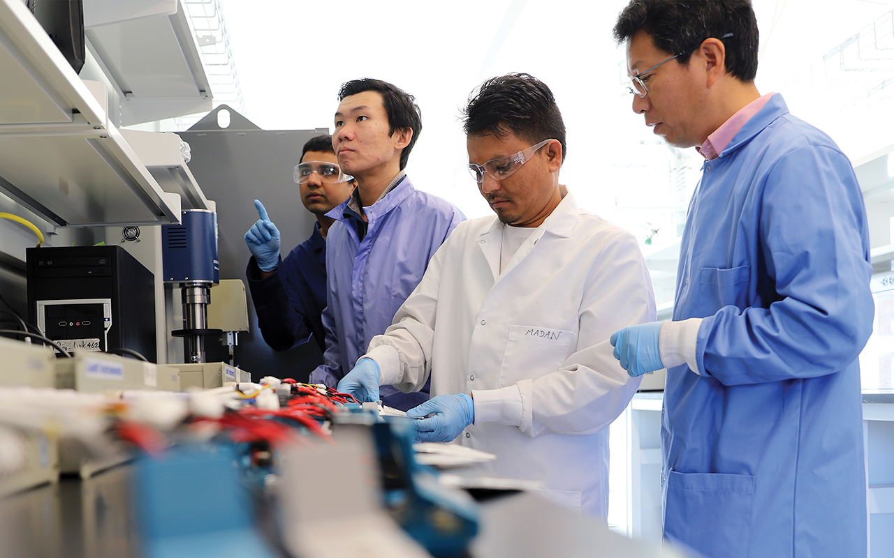 Four men wearing lab coats standing behind a counter.