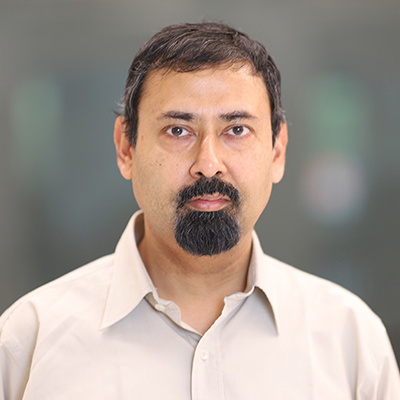 A man with dark hair and a goatee, and wearing a beige dress shirt. 