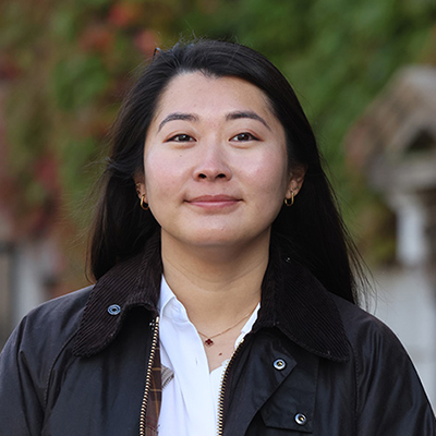 A woman with dark long hair wearing a black jacket over a white shirt.