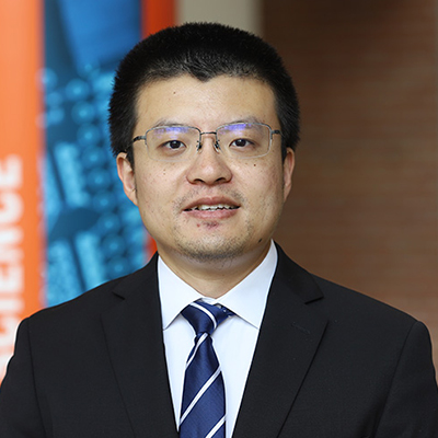 A man with dark hair wearing glasses, a dark suit, and a blue and white stripped tie.