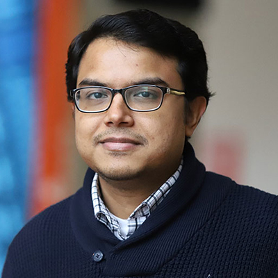 A man dark hair, glasses, and wearing a heavy navy blue sweater.