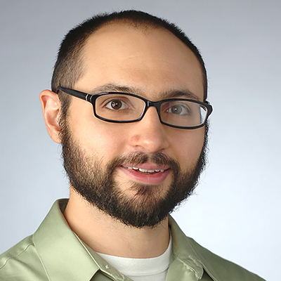 A man with a shaved head who is wearing glasses and a green shirt.