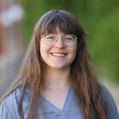 A woman with long brown hair, and wearing glasses and a grey tee shirt.
