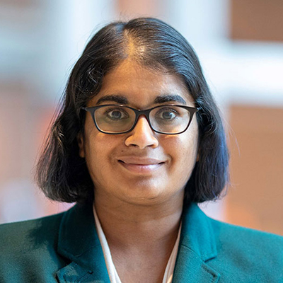 A woman with medium length dark hair, and wearing a green blazer.