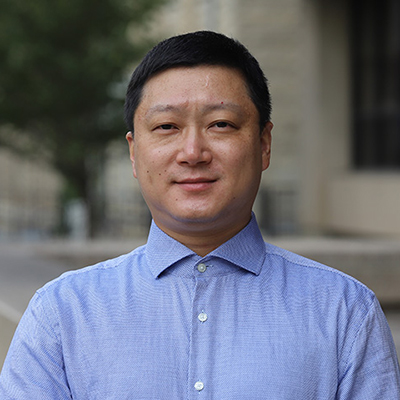 A man with short dark hair wearing a blue dress shirt.