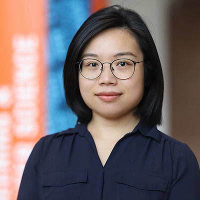 A woman with medium length dark hair, and wearing glasses and a navy blue blouse.