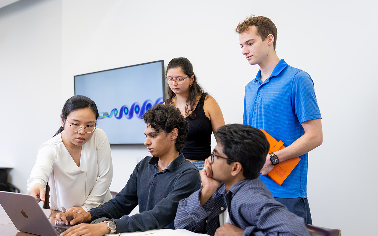 Two women and three men looking at an open laptop.