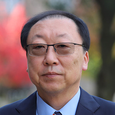 A man with dark hair wearing glasses, and a suit with a tie.