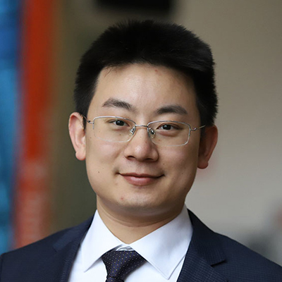 A man wearing glasses, and a dark suit and tie with a white shirt.