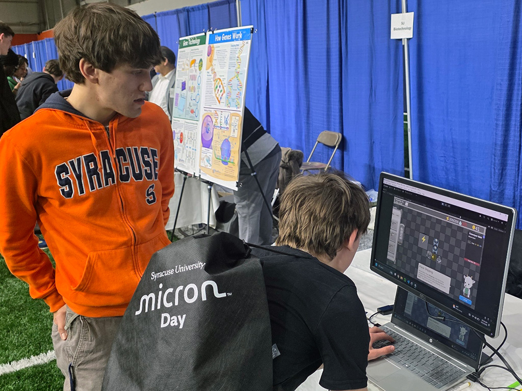 A Syracuse University student showing a student how to play a custom built microchip manufacturing video game