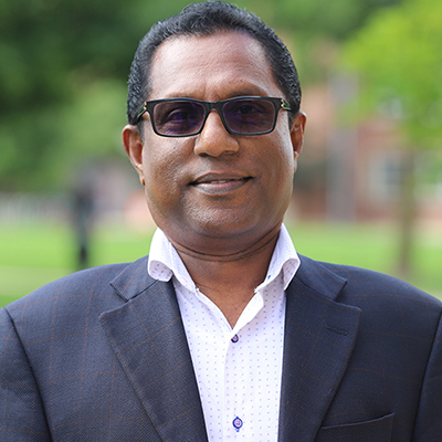 A man wearing dark glasses and black suit with white shirt.