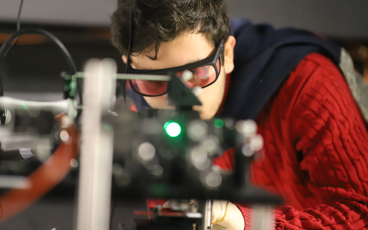 A student wearing safety glasses looking at a piece of lab equipment.