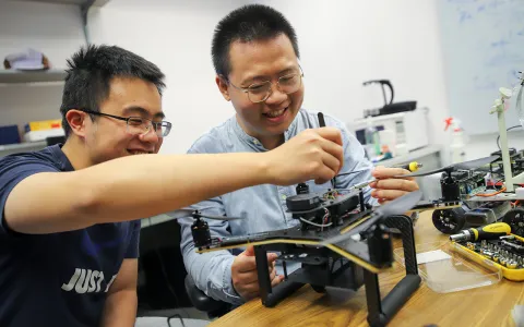 Two men using a screwdriver to work on an electronic piece of equipment.