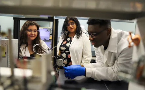 Two women and one man looking at a 3D printer.