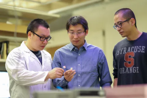 Three men examine a plastic material.